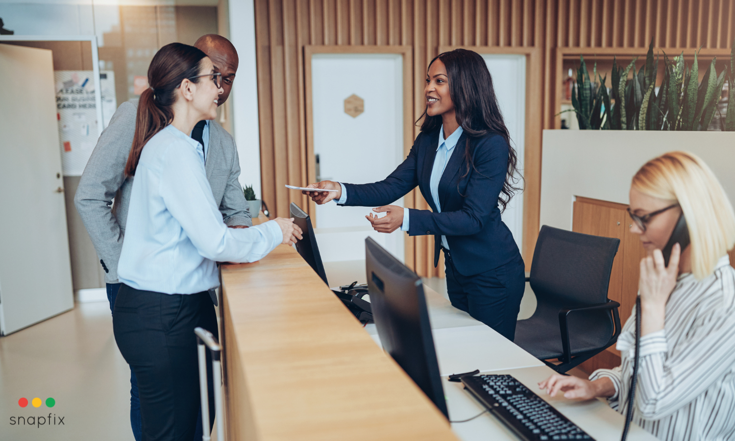 Hotel front desk staff welcoming guests at check-in, with one receptionist handing over a key card and another on the phone, representing efficient hotel operations